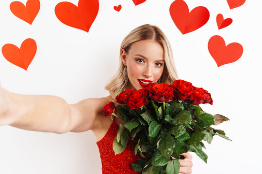 Sensual nice girl in red dress holding roses and taking selfie photo