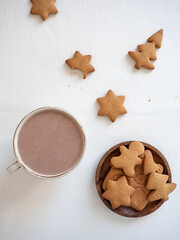 Gingerbread cookies of different shapes on a white table and in a wooden plate with a cup of cocoa in the morning light, top view