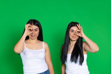 Twin girls on a green background. The girls show everything okey smiling cute.