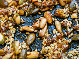 Assorted seeds being fried in oil in a frying pan