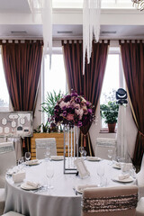 A composition of flowers and green is on a festive table at the wedding banquet hall. Stands candles. Close up.
