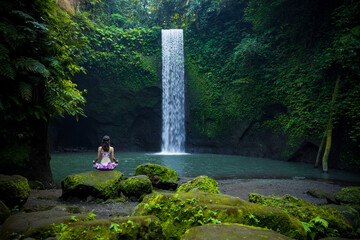 Young Caucasian woman meditating, practicing yoga at waterfall. Lotus pose. Hands in gyan mudra....