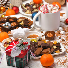 sweet food top view background for merry christmas or new year holiday decoration - chocolate candies, tangerines, cookies, marshmallow and cocoa latte on white wood