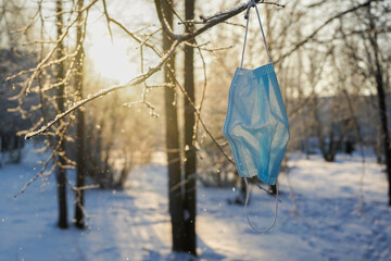 Used medical mask hanging on a tree branch, winter