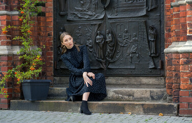 A girl in a black dress sits on the steps of an old building