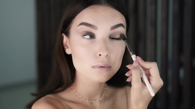 Charming brunette woman paints her eyes with brush and eyeshadows