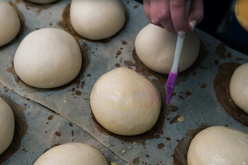 Fototapeta na wymiar Close-Up of fresh Hamburger Buns, dough. bakery products. production and cooking. Silicone and plastic brush with an egg. Woman hands