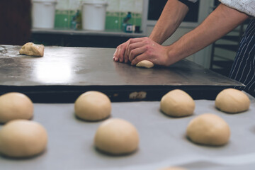 Obraz na płótnie Canvas The man is kneading the dough. Hamburger buns. Bakery, production. Copy space. Selective focus