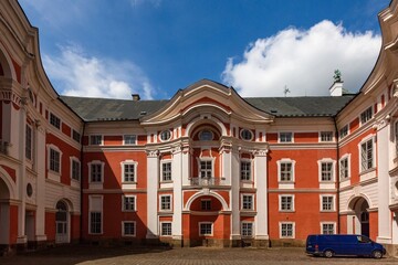 Fototapeta premium Broumov, Czech Republic - June 17 2020: Courtyard of the famous Benedictine monastery with red and white facade. Sunny summer day with blue sky and white clouds.
