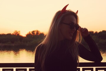 Sexy blonde lady in sunglasses like a devil over sunset background