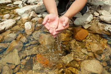 hands grasping cool crystal clear water from a rocky stream on a sunny day. the water falling...