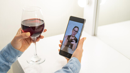 The women talk over video communication on the phone and drink red wine. The quarantined girl is not making a video call