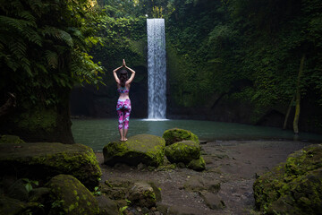 Woman standing on the rock, practicing yoga. Young woman raising arms with namaste mudra near...