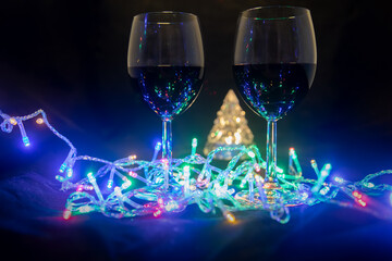 two glasses on the background of a shining Christmas tree and a multi-colored garland on a dark night background. New Year celebration.