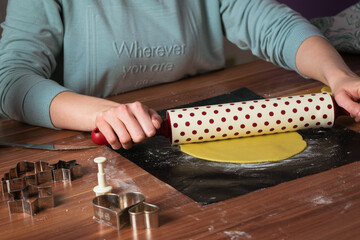 Young woman preparing christmas cookies on black baking sheet on table with dough roller 