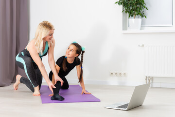 young mother and daughter are engaged in stretching on a laptop online at home during quarantine or lockdown