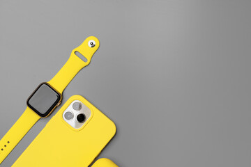 Yellow smartphone, smartwatch and earphones on gray background