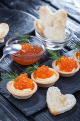 tartlets with butter and red caviar and dill on a black wooden table. Delicious snack