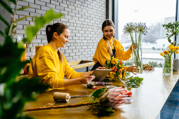 Two smiling female florists working behind counter in modern loft interior of floral shop.
