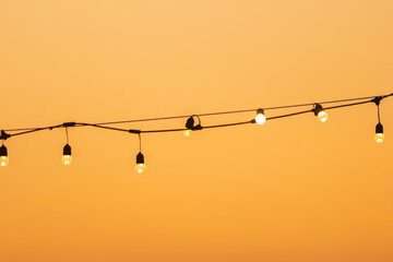 Vintage warm light bulbs on string wire at sunset.