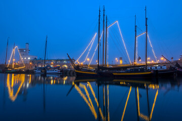 Fototapeta na wymiar Decorated traditional sailing ships in the harbor from Harlingen in the Netherlands in christmastime at night