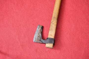An axe stays on red carpet. Metal cutting side and handle made of wood. There is corrosion on...