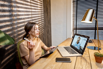 Young woman in domestic suit having a video connection with colleagues, working on laptop from a cozy home office