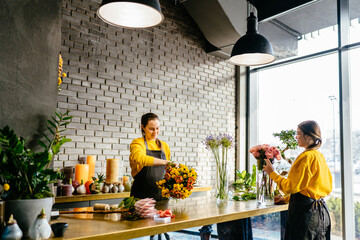 Two smiling females florists holding bouquets for orders and standing on different sides of the...