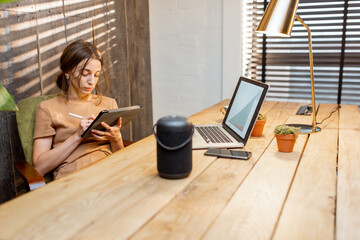 Woman working on the digital tablet at cozy home office. Smart speaker on the table. Concept of a...