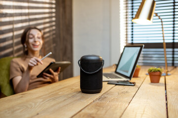 Woman talking to the smart speaker while working on the digital tablet at cozy home office. Concept of a smart home and Artificial Intelligence