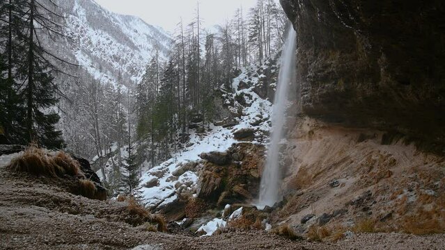 Waterfall Pericnik in Slovenia. Water plunges in waterfall base. Famous path under waterfall. Snow covering nature in winter season in Alps mountains. Static shot, real time, wide angle