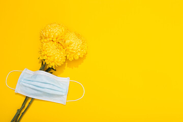 Bright bud of chrysanthemum and medical mask on a yellow background with copy space. Banner with flowers in a minimalist style. Delicious aroma and pollen of plant. Hello spring, summer time. Allergy
