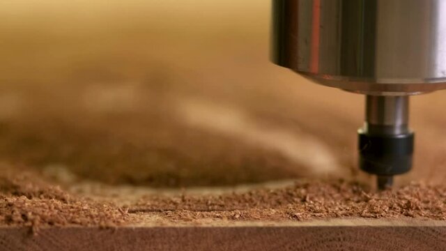 head of the CNC machine cuts out a wooden decorative thing. camera follows her. Splinters fly in different directions