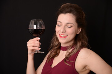 girl with red lips in a Marsala dress holding a glass of red wine in her hands on a black background