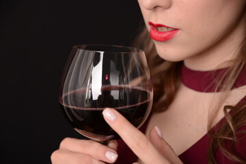 girl with red lips in a Marsala dress holding a glass of red wine in her hands on a black background