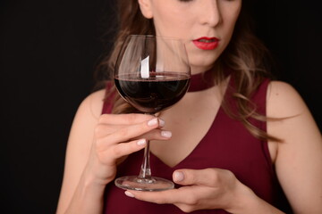 girl with red lips in a Marsala dress holding a glass of red wine in her hands on a black background