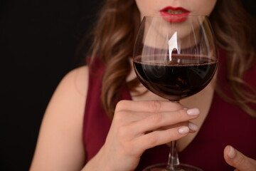 girl with red lips in a Marsala dress holding a glass of red wine in her hands on a black background