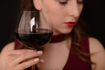 girl with red lips in a Marsala dress holding a glass of red wine in her hands on a black background