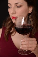 girl with red lips in a Marsala dress holding a glass of red wine in her hands on a black background