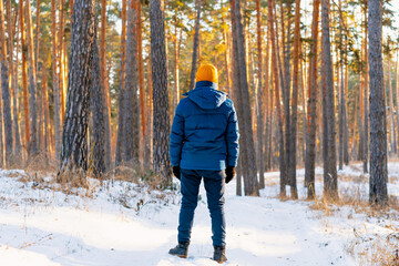 Rear view of young man in yellow hat on the background of a snowy landscape in a winter pine forest