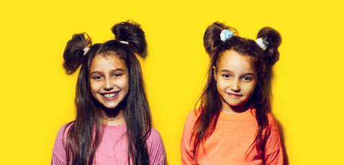 Obraz premium Studio portrait of two cheerful teenage girls on background of yellow color.