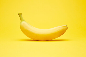 Single fresh raw clean isolated one alone horizontally oriented yellow banana on the bright solid...