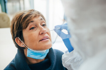 Close up of the face of senior female patient being tested for Covid-19 with a nasal swab, by a health Professional protected with gloves and PPE suit. Rapid Antigen Test during Coronavirus Pandemic.