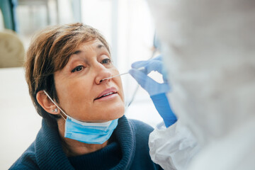 Close up of the face of senior female patient being tested for Covid-19 with a nasal swab, by a...