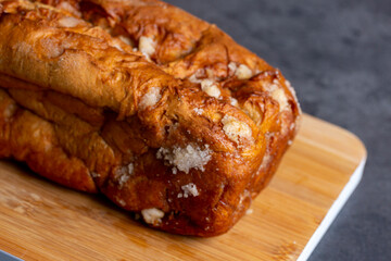 Sugar on solid orange brown Sugarloaf bread closeup with wooden cutting board against a gray surface background