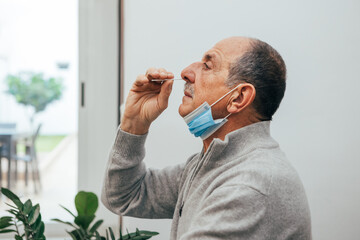 Senior man sitting, self test for COVID-19 at home with Antigen test kit. Coronavirus nasal swab...