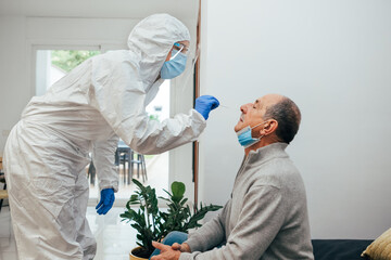 Health Professional in PPE suit and face shield introducing a nasal swab to a senior adult patient...