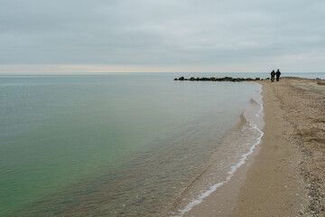 Sea and sky in winter. Minimalistic landscape. Men walk on a lonesome coast.