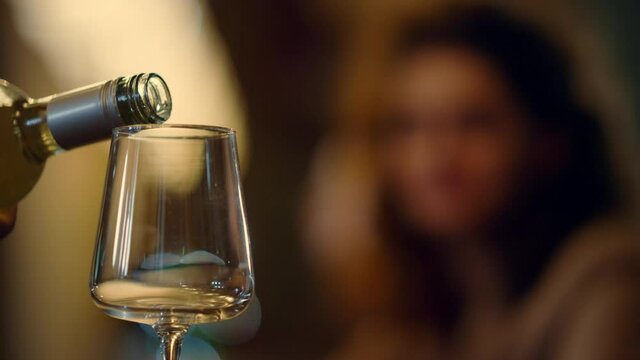Unknown bartender pouring wine from bottle. Blurred woman taking glass indoors.