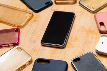 Pile of multicolored plastic back covers for mobile phones on wooden background with a phone on the side